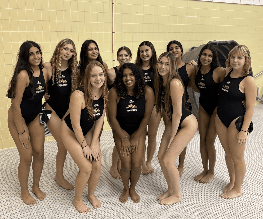 Smiling women's swim team in black swimsuits posing together on pool deck.