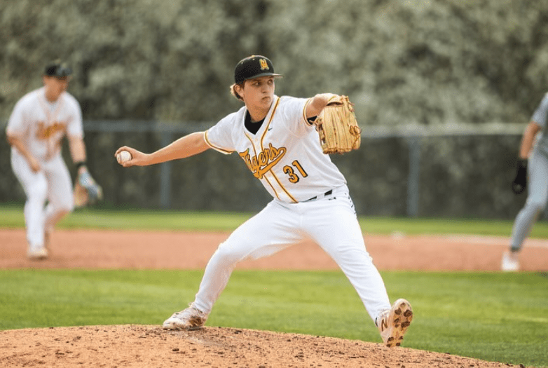Baseball pitcher in action on the mound during a game, wearing a white uniform with Tigers text.