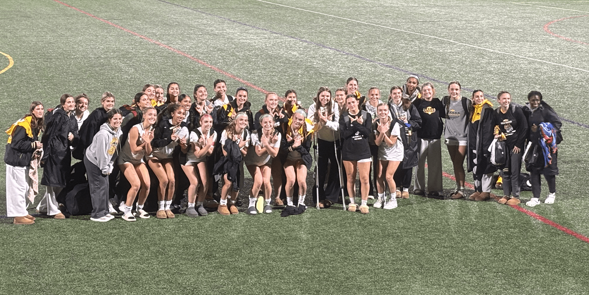 Group of young athletes posing on a sports field, smiling after a game, wearing matching team outfits.
