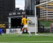 Goalkeeper in yellow jersey prepares to throw the ball during a soccer match.