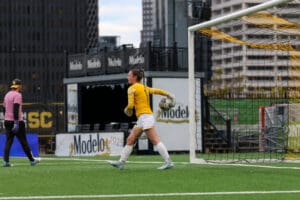 Goalkeeper in yellow jersey prepares to throw the ball during a soccer match.