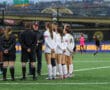 Soccer team huddle with coach and referees on the field before a match, discussing strategy and rules.