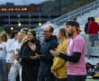 Coaches and players clapping and cheering on the sideline during a soccer game, with a blurred stadium backdrop.