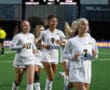 Female soccer team celebrating on the field, wearing white uniforms with numbers 11, 9, and 7 visible.