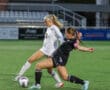 Two female soccer players competing for the ball during a game on a green field.