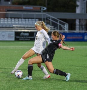 Two female soccer players competing for the ball during a game on a green field.