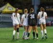 Four female soccer players on field in uniform, walking together before a game, with focus on teamwork and sportsmanship.