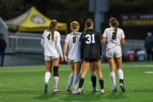 Four female soccer players on field in uniform, walking together before a game, with focus on teamwork and sportsmanship.