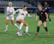 Women's soccer match, players compete for possession of the ball on a field under stadium lights.