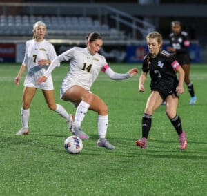 Women's soccer match, players compete for possession of the ball on a field under stadium lights.