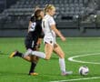 Two female soccer players in action during a night game on a green field.