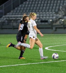 Two female soccer players in action during a night game on a green field.