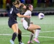 Two female soccer players in action, competing for the ball on a field during a nighttime match.