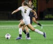 Soccer player in white jersey number 2 dribbles past opponents during nighttime match on green field.