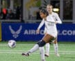 Soccer player in white uniform kicks ball during a match on a green field at night.
