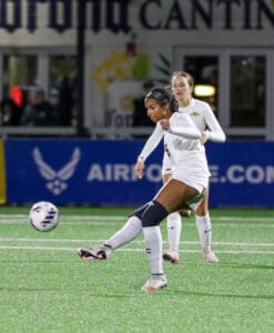 Soccer player in white uniform kicks ball during a match on a green field at night.