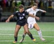 Two female soccer players competing intensely for the ball on a field during a match.