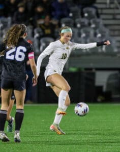 Soccer players in action, one in white kit controlling the ball during a match on a green pitch.