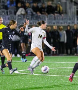 Soccer player in white dribbles past opponent in black during a night match on a green field.