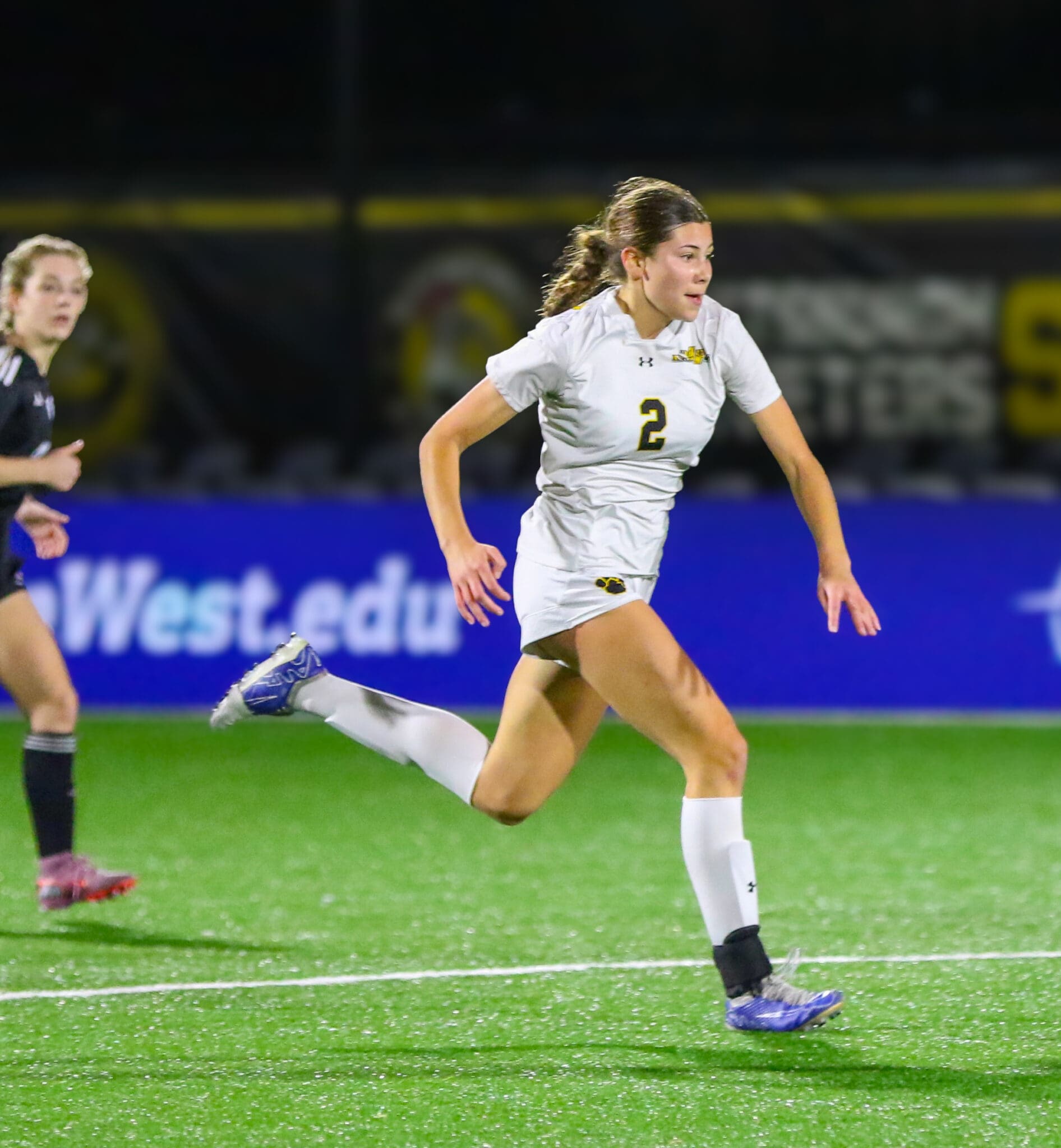 Soccer player in white jersey running on field during a night match, focused and determined.