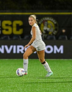 Soccer player in action on the field during a night game, wearing a white uniform, focused on controlling the ball.
