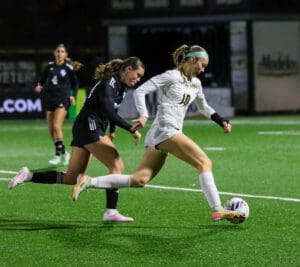 Soccer player in white dribbling past opponent on field during a night match.