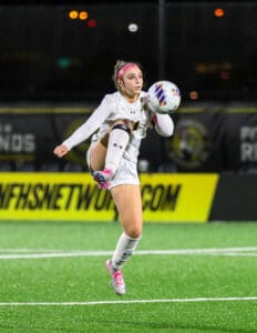 Soccer player in action, kicking ball mid-air on field at night game.