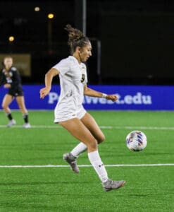 Soccer player in white uniform controlling the ball mid-air on a brightly lit field during a night match.