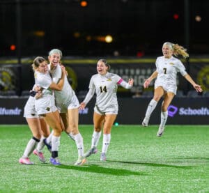 Soccer players in white uniforms celebrating a victory on the field at night.
