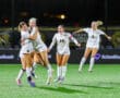 Women's soccer team celebrating a victory on the field at night, showcasing teamwork and joy.