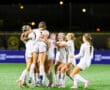Girls' soccer team celebrating a victory with joy and excitement on the field at night.