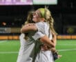 Two female soccer players joyfully embrace on the field, celebrating a victory under the stadium lights.