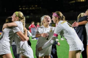 Soccer players celebrating a victory at night, sharing hugs and joy on the field.