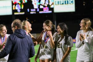 Soccer team celebrating victory with medals under scoreboard at night.