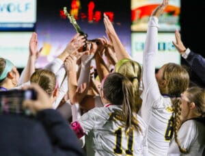 Girls soccer team celebrates with trophy under stadium lights. Teamwork and victory in sports event.