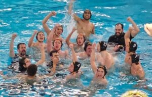 Water polo team celebrating victory in pool with arms raised and joyful expressions.