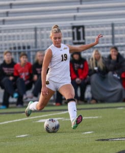Soccer player in white kit kicking ball during a match, focused on the field.