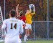 Soccer goalie in yellow jersey catches ball mid-air during a competitive match near the goal, autumn backdrop.