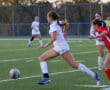 Soccer players competing on the field during a match at sunset.
