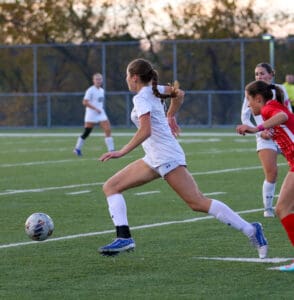 Soccer players competing on the field during a match at sunset.