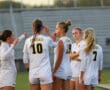 Soccer team in discussion on field during evening game, wearing numbered jerseys with Tigers on the back.