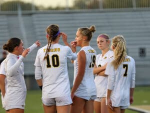 Soccer team in discussion on field during evening game, wearing numbered jerseys with Tigers on the back.