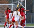 Soccer goalkeeper jumps to block a shot during a match, players in action near the goalpost.