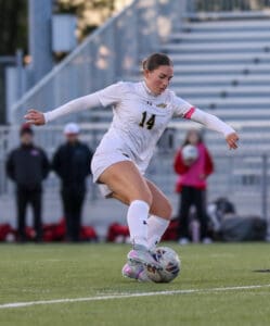 Soccer player in mid-action during a match, wearing a white uniform with the number 14, focused on controlling the ball.