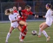 Soccer players compete for the ball during a match on a grassy field.