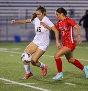 Two female soccer players competing for the ball on a green field during a match.