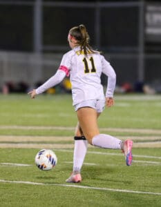 Soccer player in white uniform with number 11 dribbling the ball on a field during a night match.