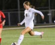 Soccer player in white jersey kicking ball on field during night match.