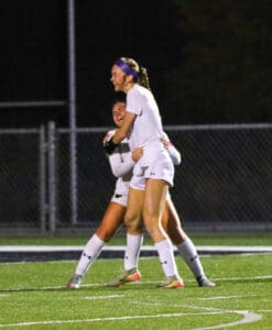 Soccer players celebrating a victory on the field in nighttime match.