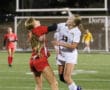 Two female soccer players competing for the ball during a match at night on a field.